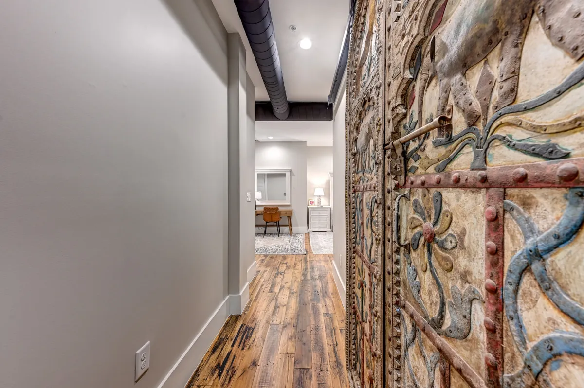 This image captures a hallway with an ornately carved door, elegant wooden flooring, a decorative rug, and a desk with a chair. The artistic details and textures create a sense of sophistication and comfort.