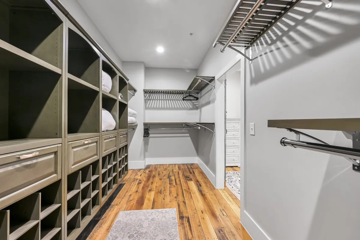 A spacious closet with custom shelving, wooden flooring, and hanging racks, offering ample space for organizing clothing and accessories.