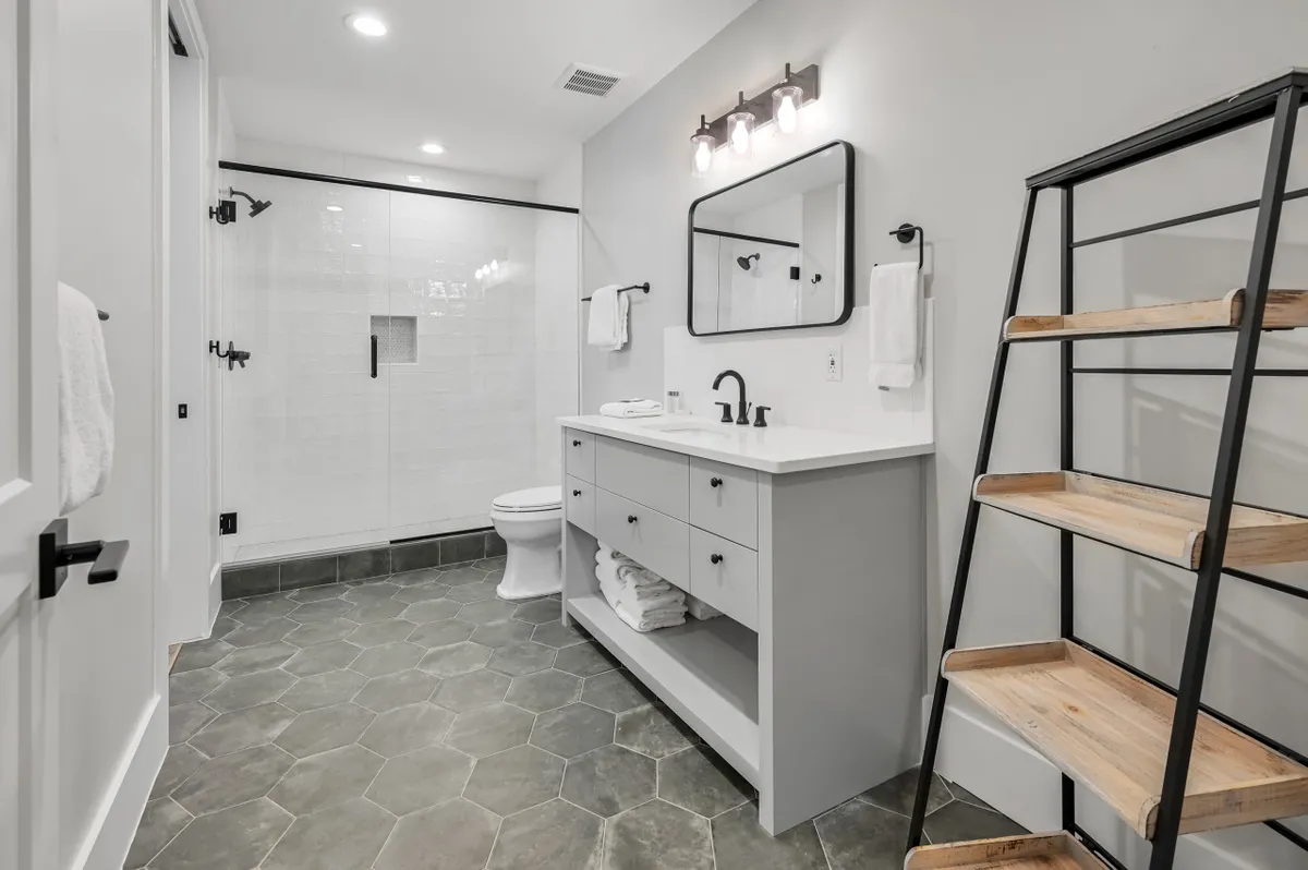 A spa-inspired bathroom with a modern vanity, sleek sink, hexagonal floor tiles, a walk-in shower, and a stylish ladder shelf for towels and essentials.